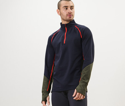 Mężczyzna ma na sobie termoaktywną bluzę funkcyjną, granatowe legginsy i pozuje.