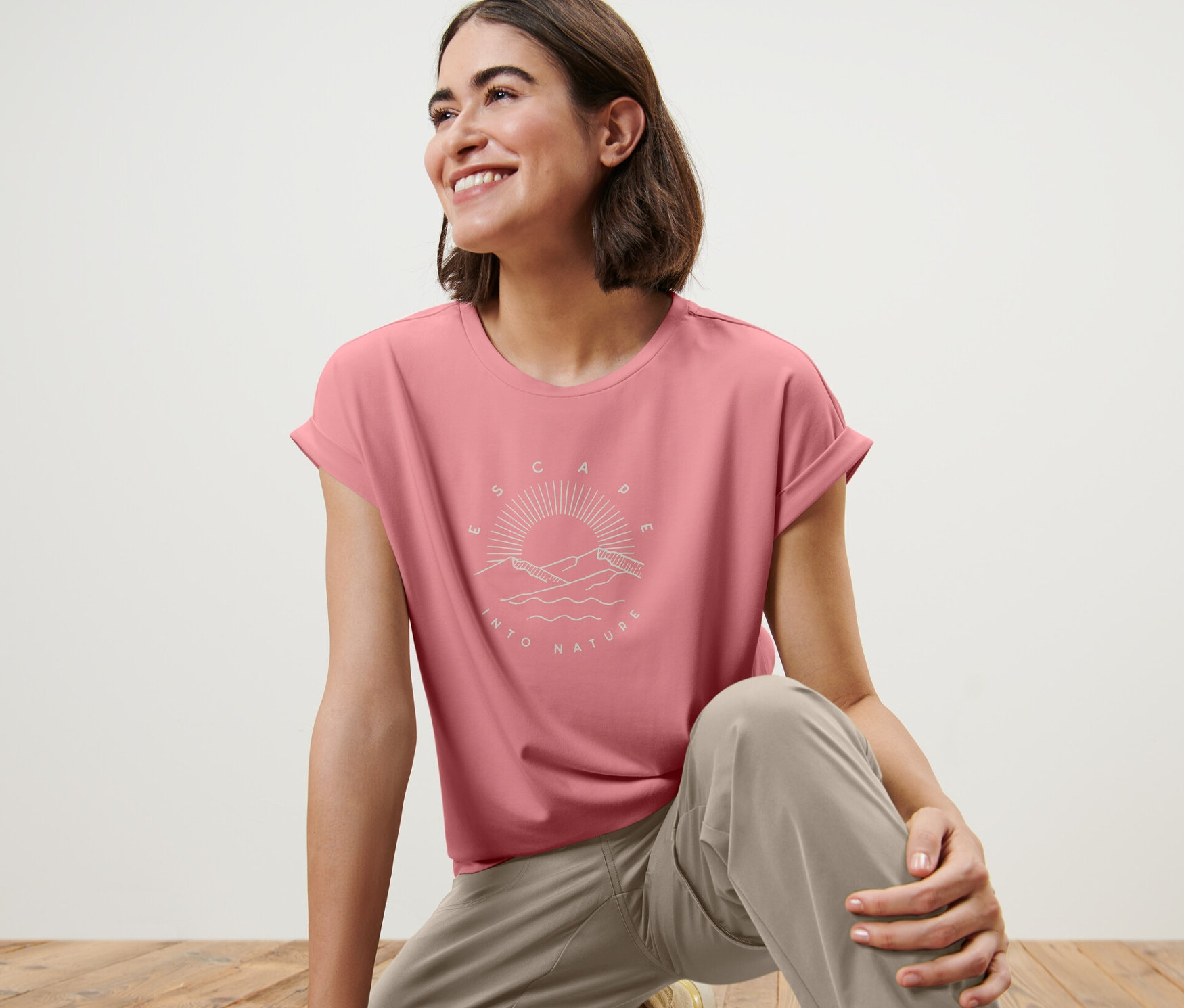 Kobieta na drewnianej podłodze ma na sobie różową koszulkę z nadrukiem.