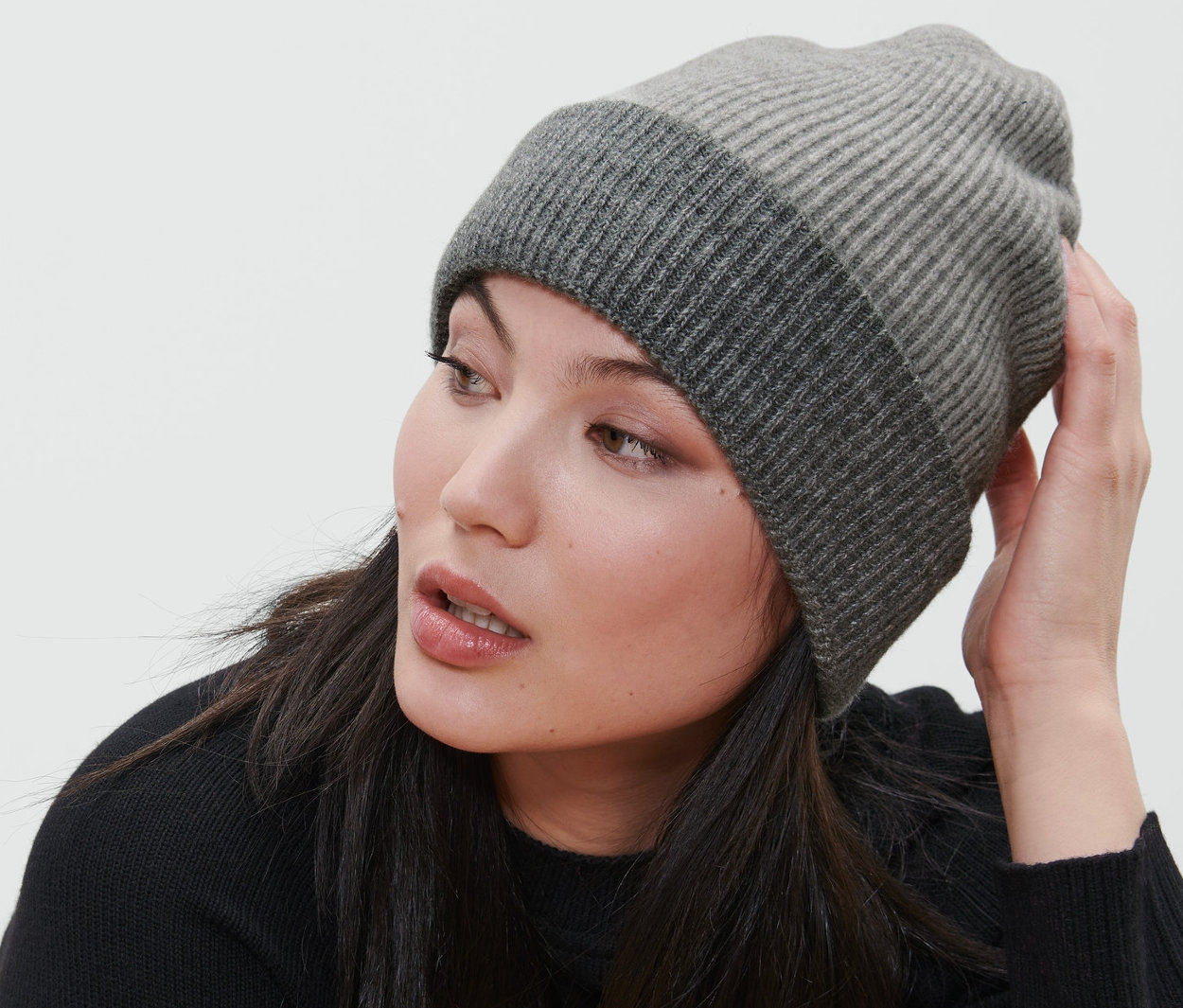 Kobieta siedzi na krześle i ma na sobie szarą czapkę dzianinową.