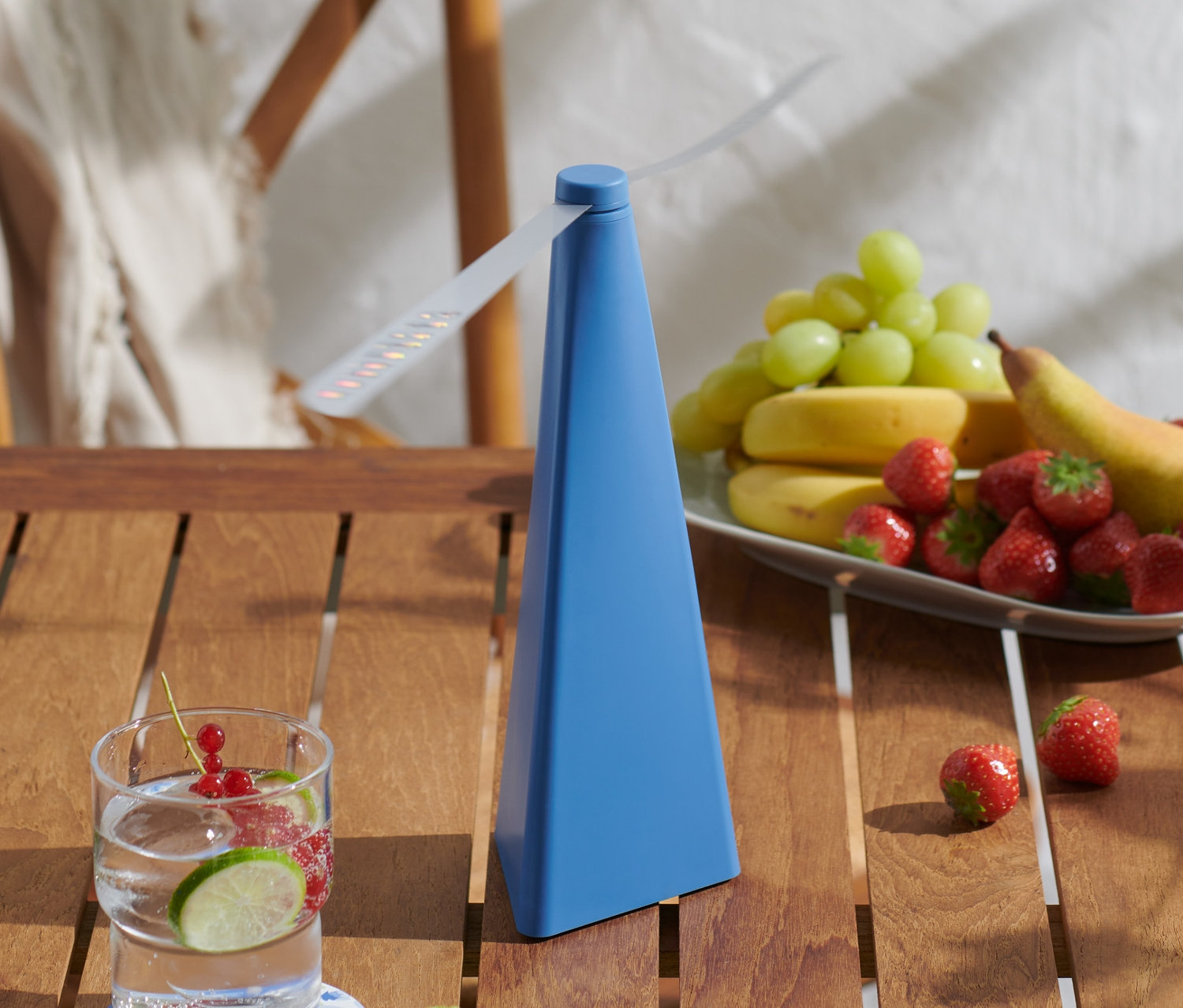 Na drewnianym stole stoi niebieski odstraszacz much, szklanka z owocami, talerz sałatki i talerz z owocami.