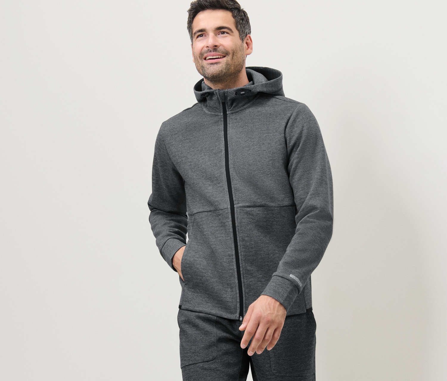 Mężczyzna ma na sobie szarą funkcyjną bluzę dresową.