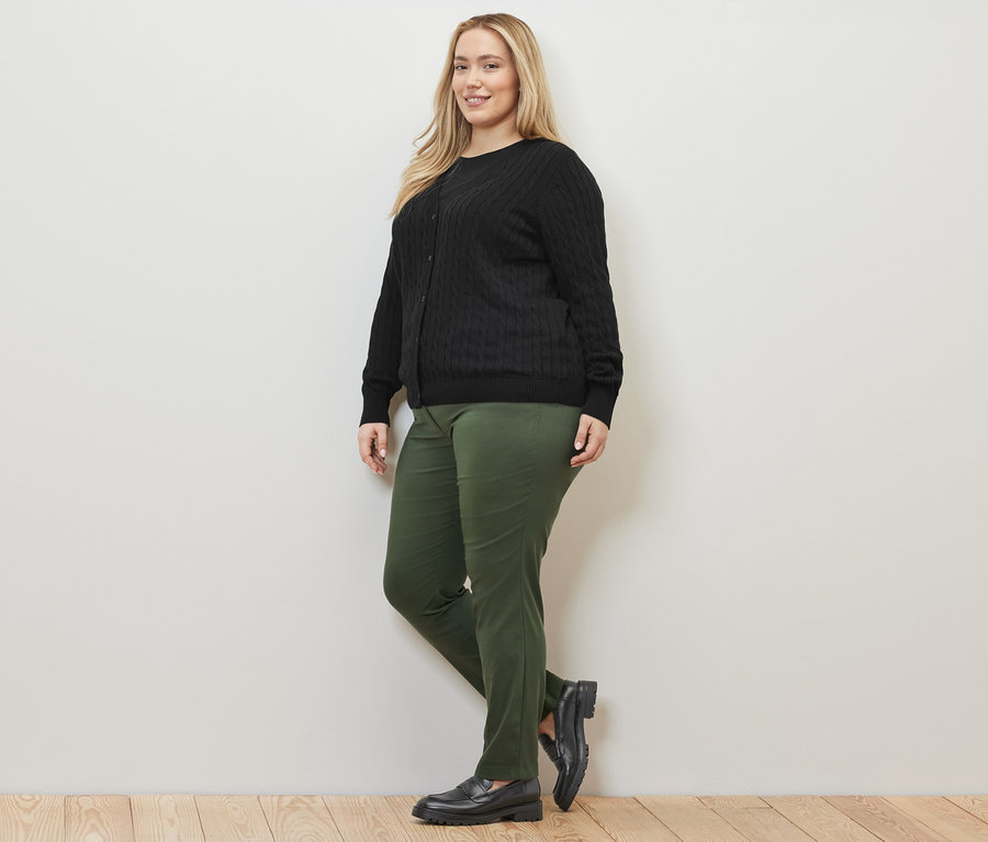 Kobieta pozuje w czarnym, cienkim kardiganie z wzorem warkoczowym i zielonych spodniach z bengaliny.