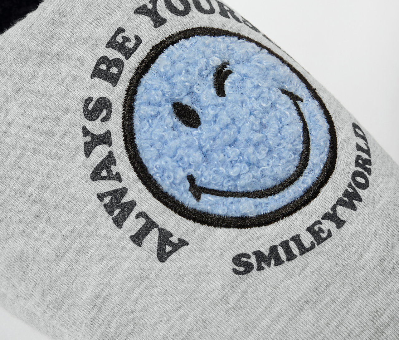 Szczegół szarego kapcia SMILEYWORLD® z niebieską uśmiechniętą buźką.