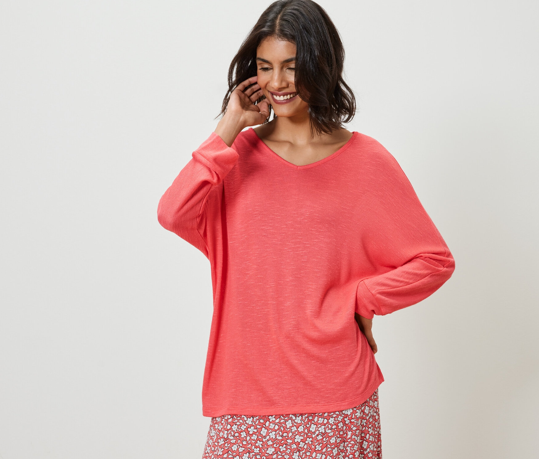 Kobieta pozuje w koralowej bluzce z rękawami typu nietoperz i kwiecistej spódnicy.