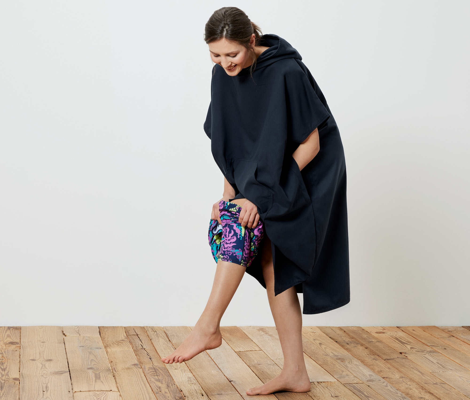 Uśmiechnięta kobieta zakłada granatowe poncho kąpielowe.