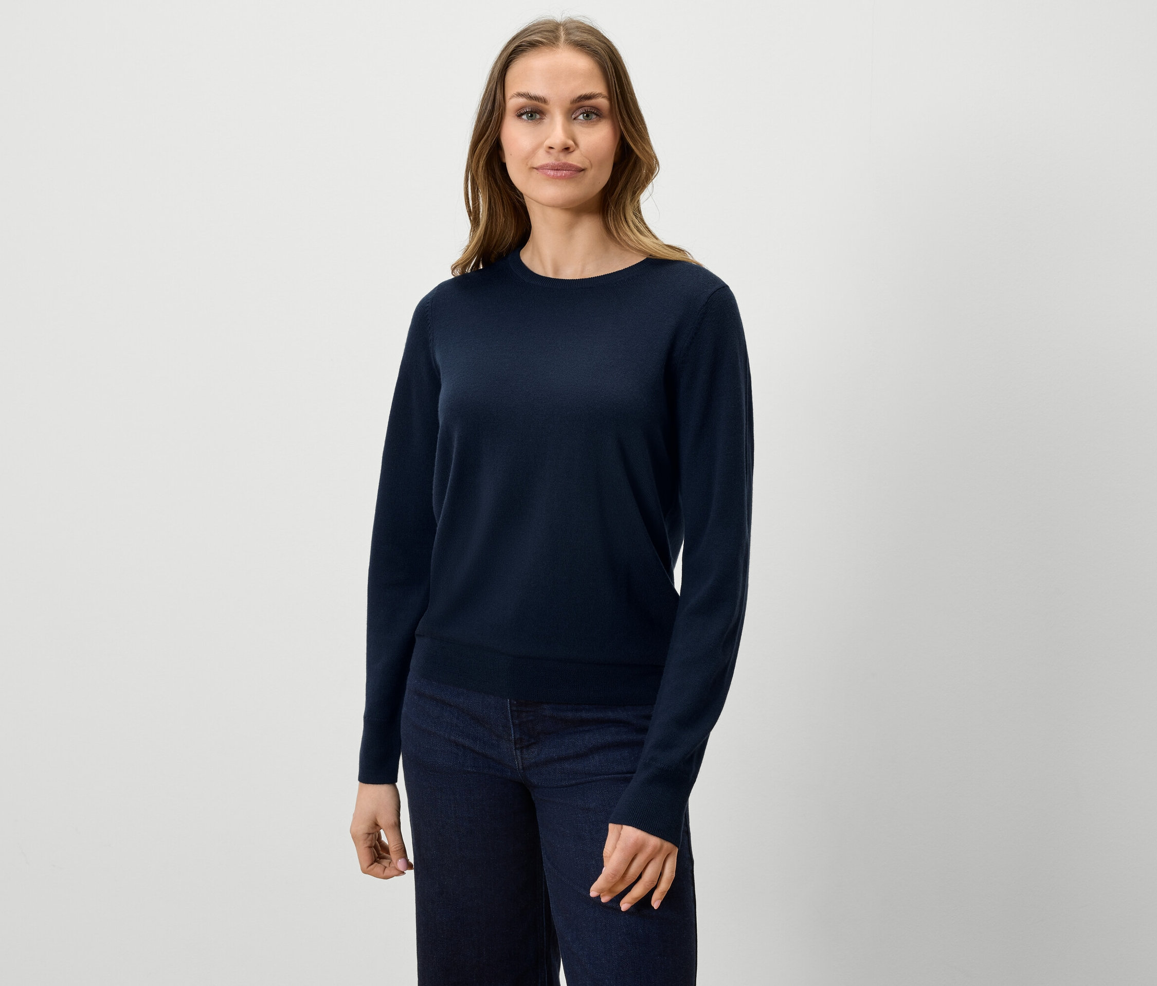 Kobieta ma na sobie granatowy sweter i dżinsy.