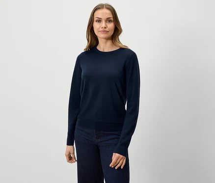 Kobieta ma na sobie granatowy sweter i dżinsy.