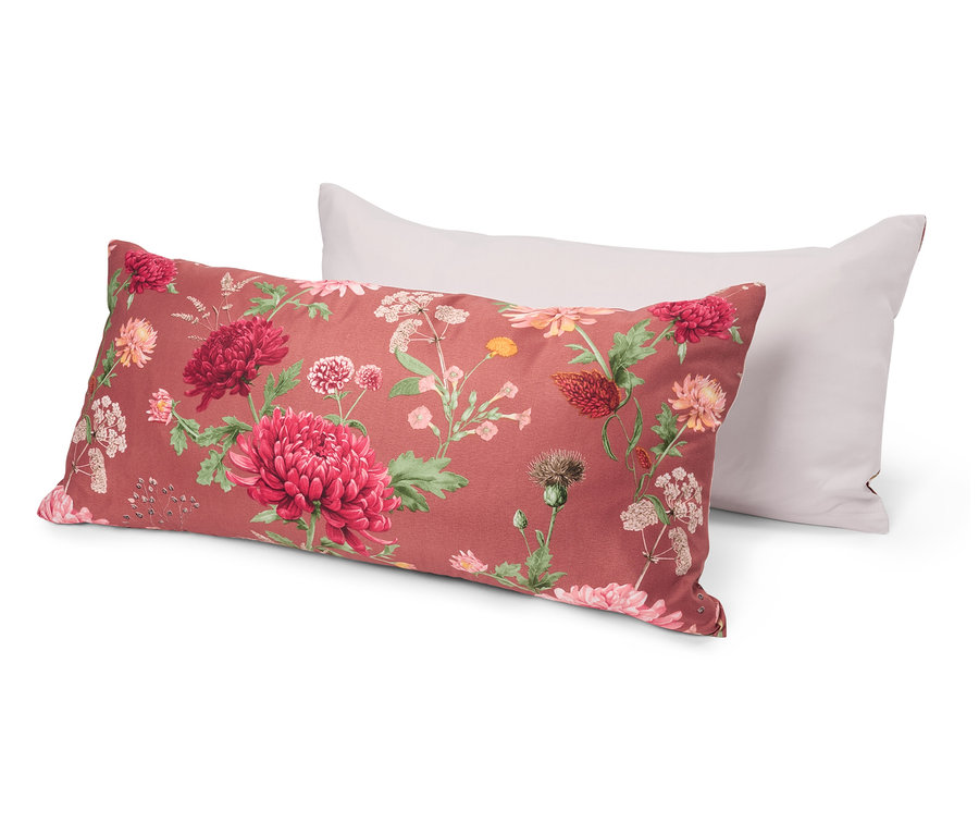 Dwie poduszki leżą na sobie. Dolna poduszka ma kwiatowy wzór z czerwonymi i różowymi kwiatami na czerwonym tle. Górna poduszka jest biała.