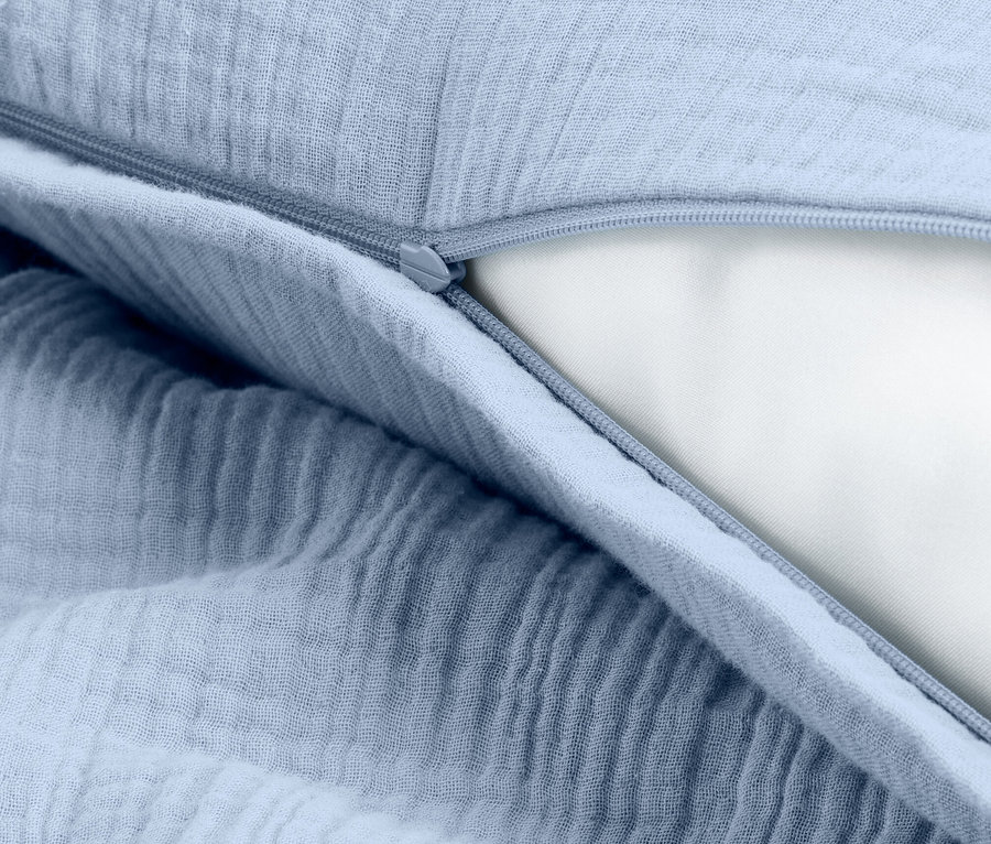 Zbliżenie na jasno-niebieską poszewkę na poduszkę z zamkiem błyskawicznym, odsłaniającą białe wypełnienie poduszki.