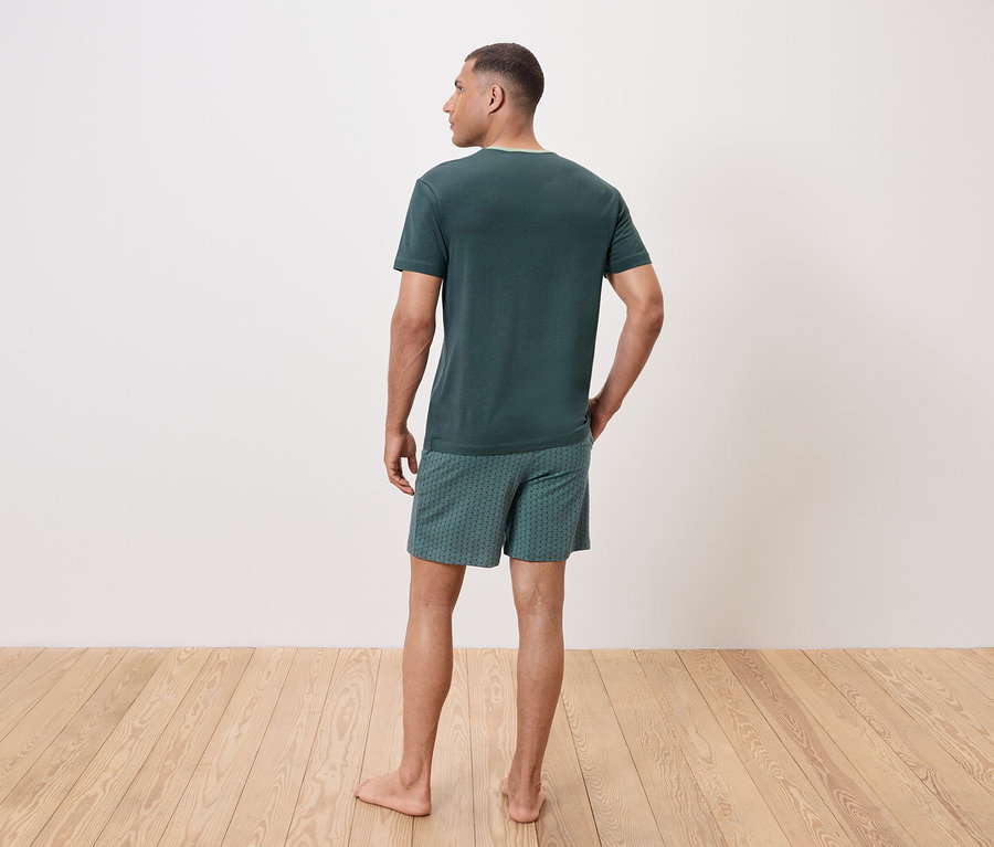 Mężczyzna tyłem do kamery ma na sobie zielony t-shirt i wzorzyste szorty.