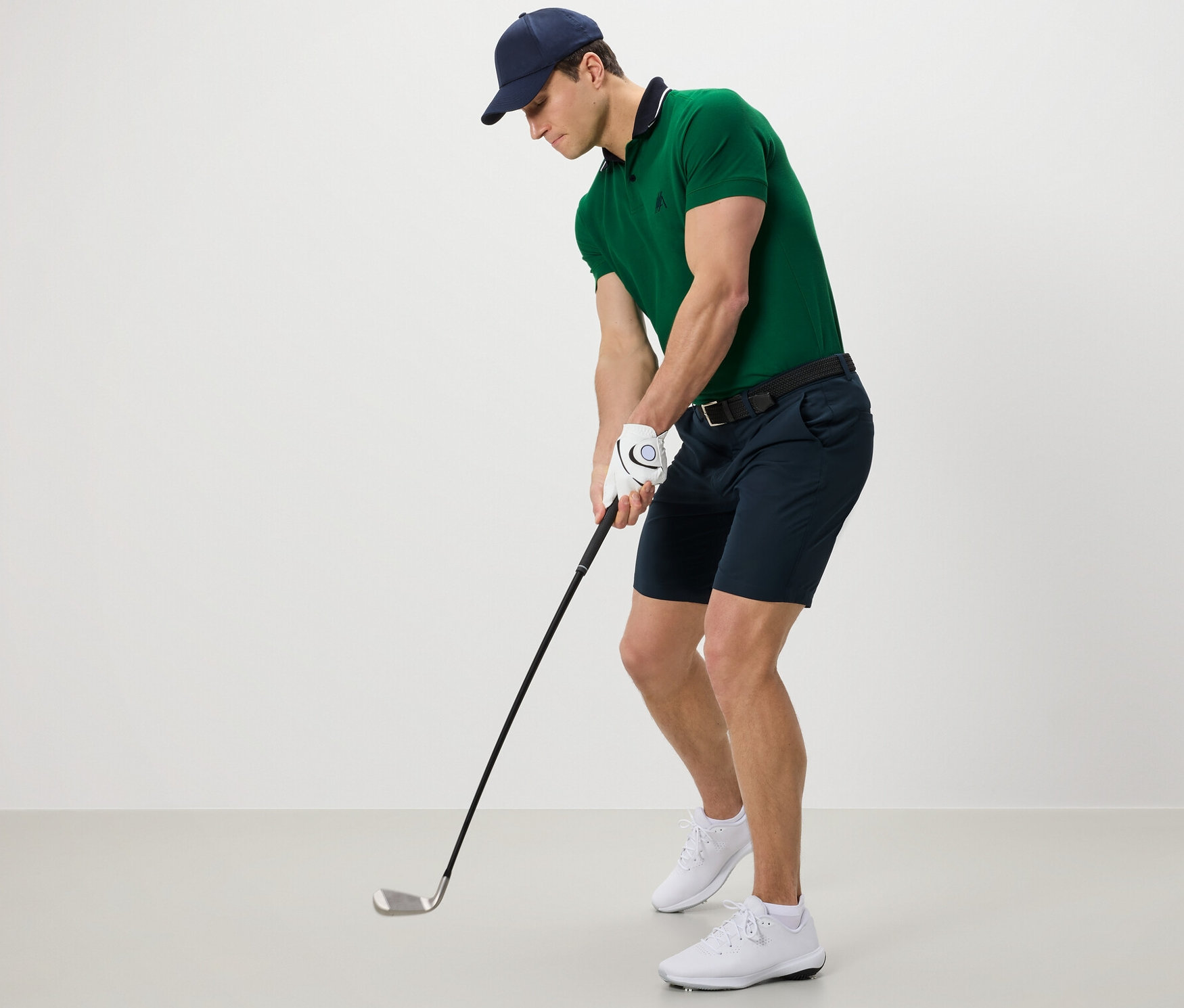 Mężczyzna w zielonej koszulce polo i szortach funkcyjnych gra w golfa.