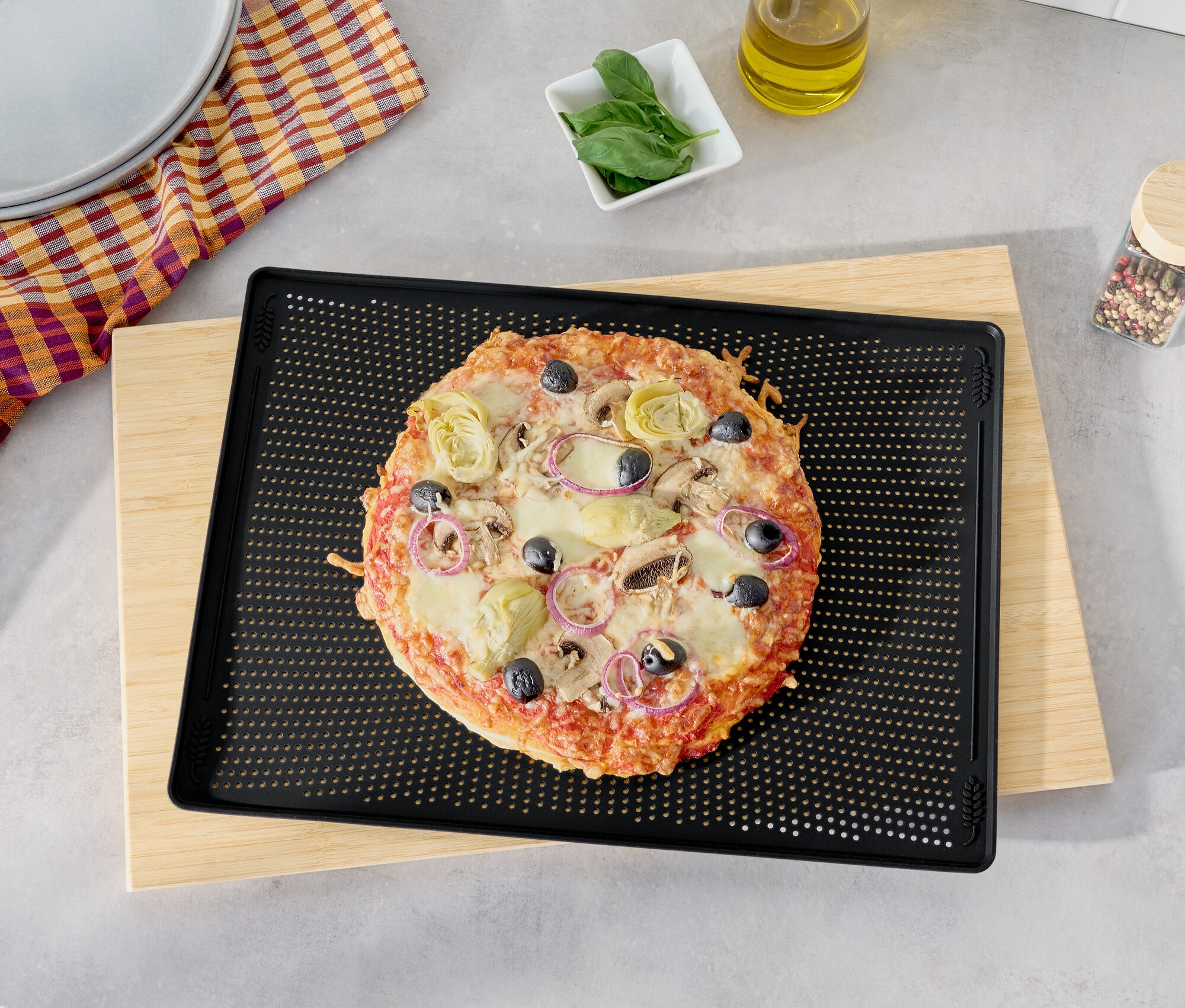 Pizza z oliwkami, karczochami i czerwoną cebulą na czarnej blasze do pieczenia na drewnianej desce do krojenia.