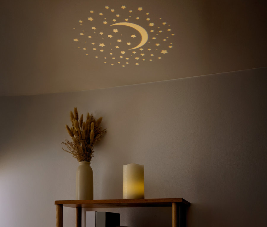 Na suficie widać gwiazdy i półksiężyc. Na półce stoi wazon z suszonymi kwiatami i świeca.