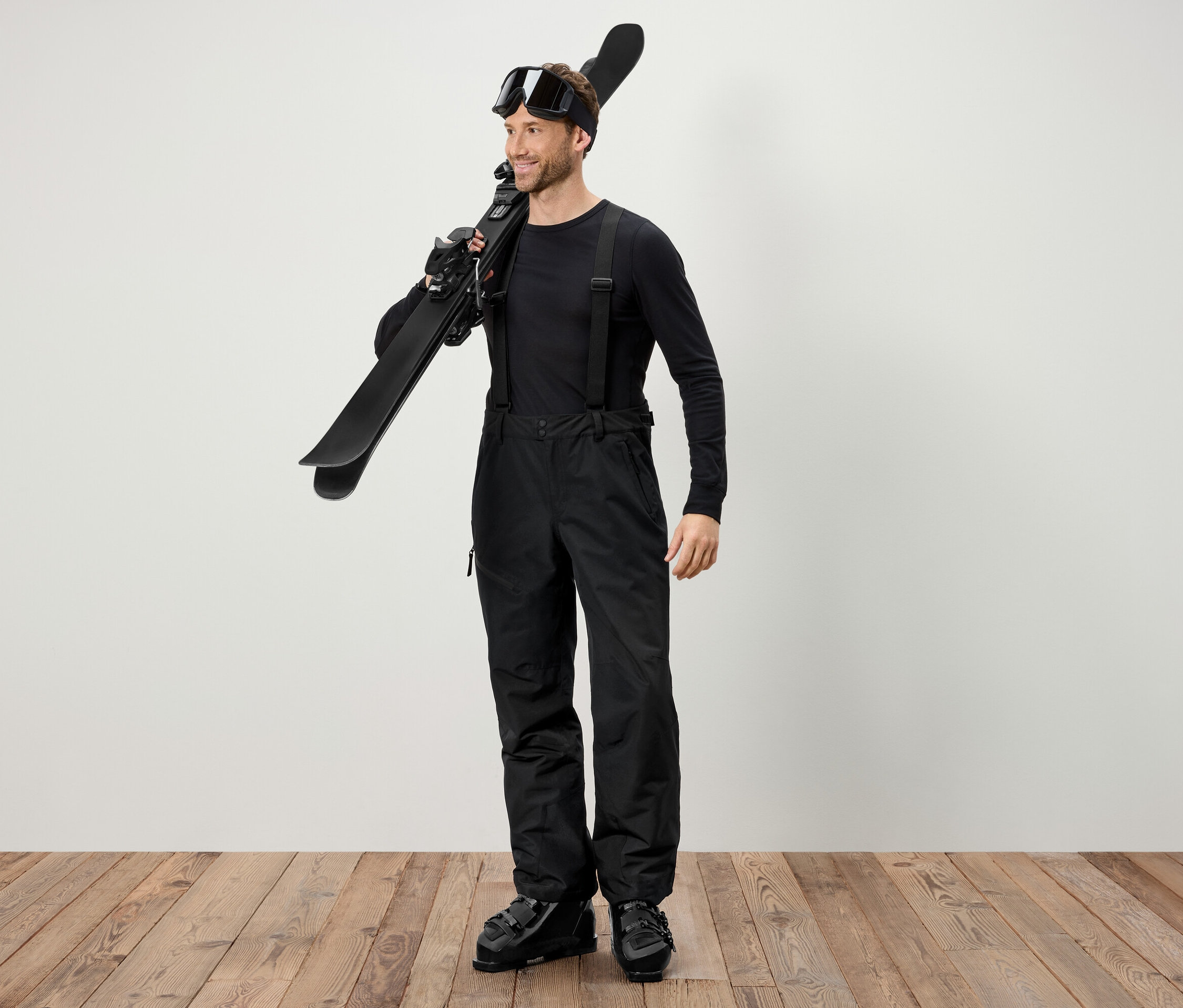 Mężczyzna w czarnym stroju narciarskim niesie narty na ramieniu.