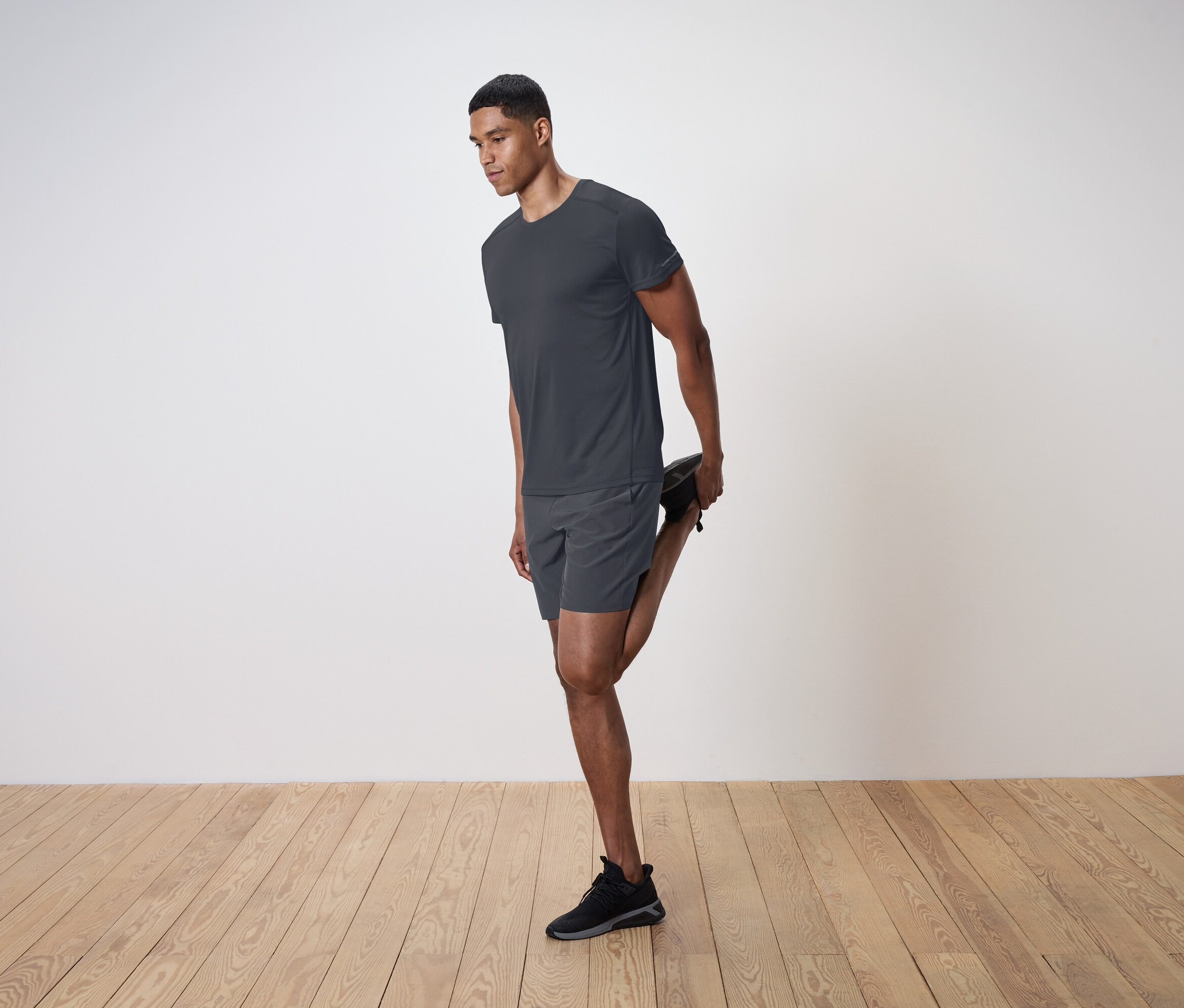 Mężczyzna rozciąga mięsień czworogłowy uda na tle białej ściany.