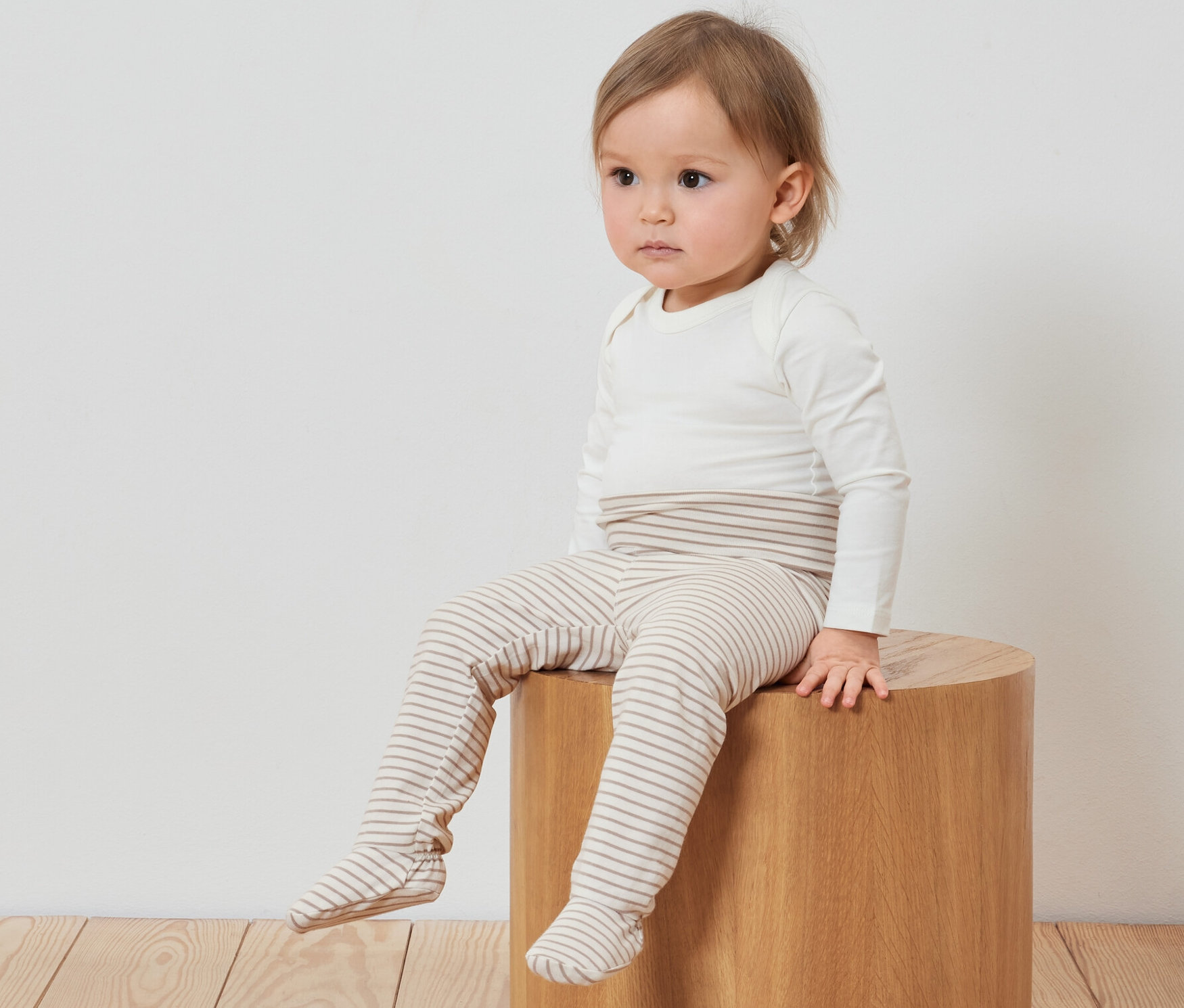 Dziecko siedzi na drewnianym stołku i ma na sobie 3 pary spodni niemowlęcych.