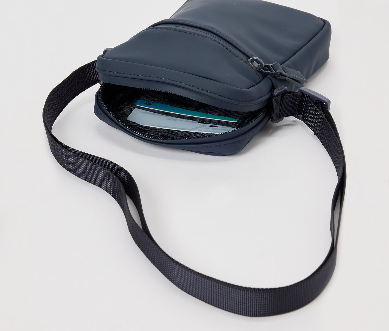 Granatowa, przeciwdeszczowa torebka na ramię z czarnym paskiem i kartami w środku.