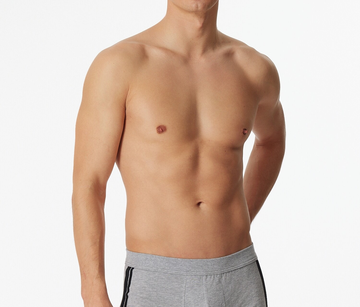 Mężczyzna pozuje bez koszulki w jasno szarych bokserkach SCHIESSER z melanżem i czarnym paskiem z boku.