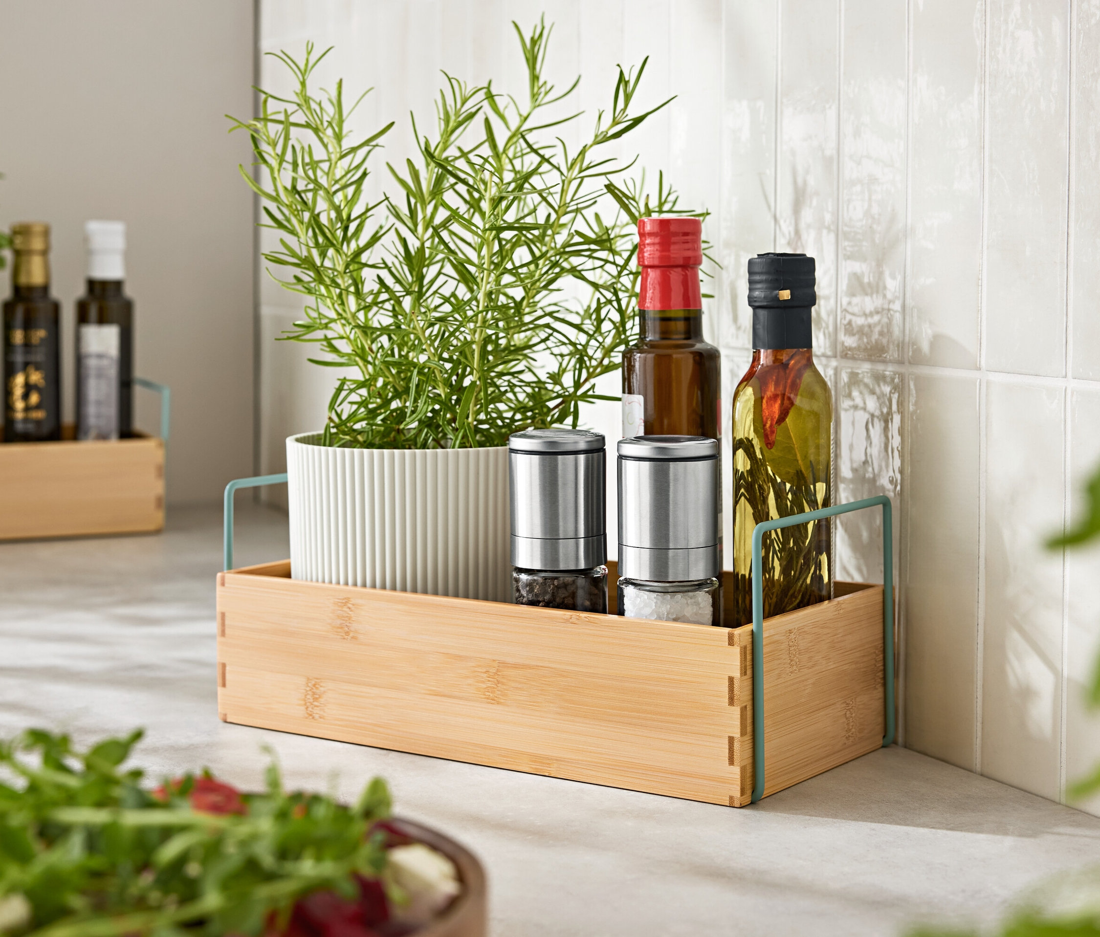 Zioła w doniczce, dwa młynki do przypraw i dwie butelki oleju na drewnianej tacy.