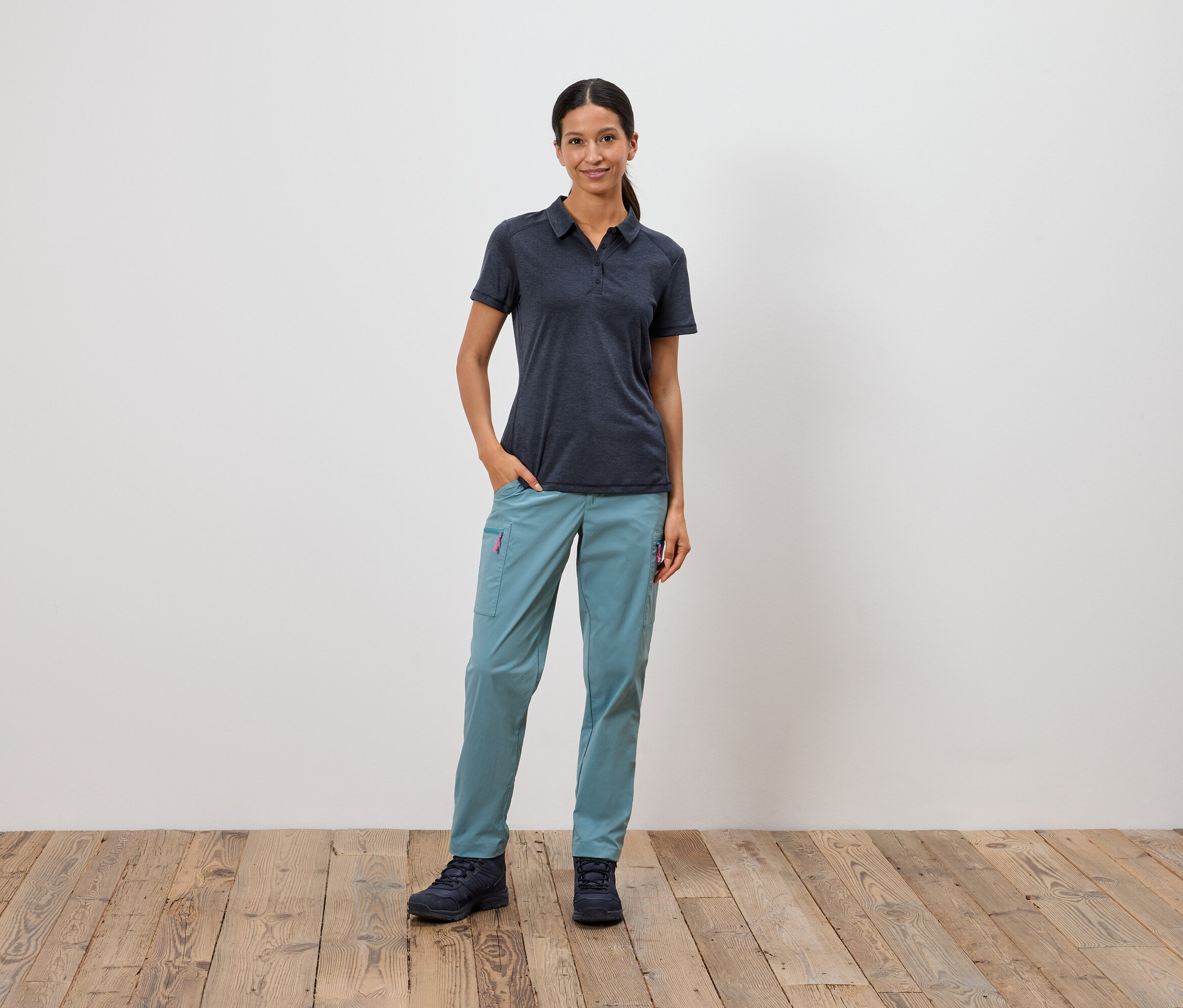 Kobieta stoi z ręką w kieszeni na tle białej ściany.