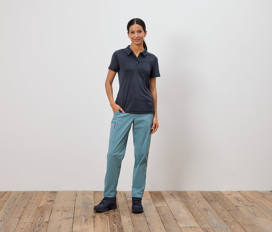 Kobieta stoi z ręką w kieszeni na tle białej ściany.