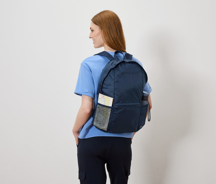 Kobieta od tyłu z granatowym plecakiem, w którym znajduje się mapa i butelka z wodą.