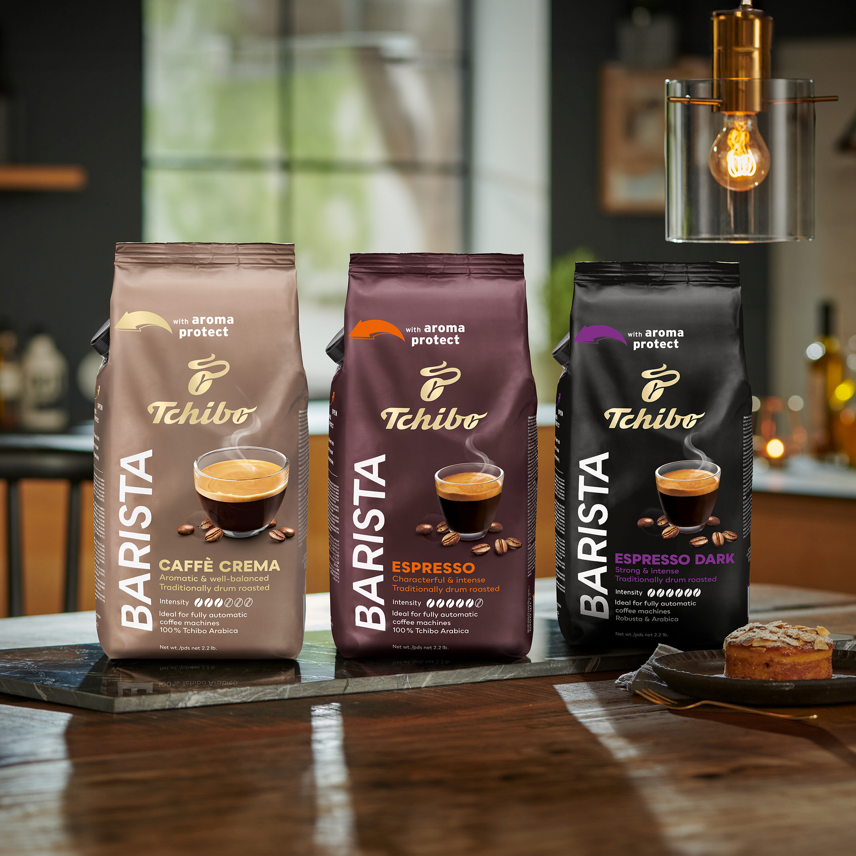 Trzy opakowania kawy ziarnistej Tchibo Barista stoją na stole, od lewej do prawej: Caffè Crema, Espresso i Espresso Dark.