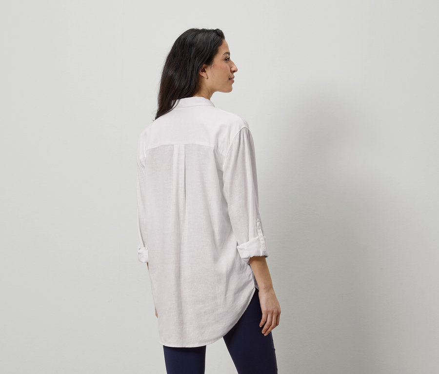 Kobieta od tyłu w białej koszuli i niebieskich legginsach.