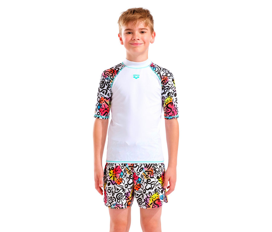 Chłopiec o blond włosach ma na sobie białą koszulkę Arena z kolorowymi rękawami i pasujące szorty.