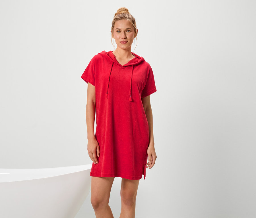 Kobieta stoi obok wanny i ma na sobie czerwoną sukienkę z krótkim rękawem i kapturem.