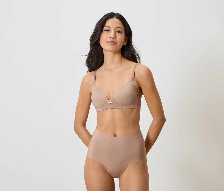 Kobieta ma na sobie beżowy biustonosz i majtki na białym tle.