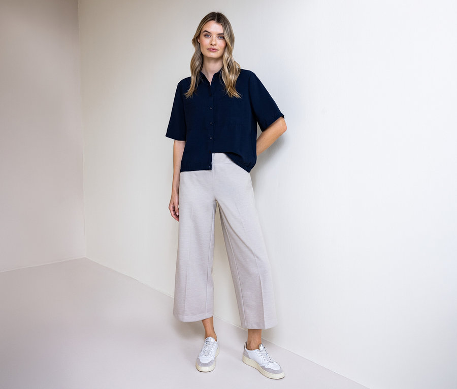 Kobieta w spodniach i koszuli Street One. Stoi na tle ściany.