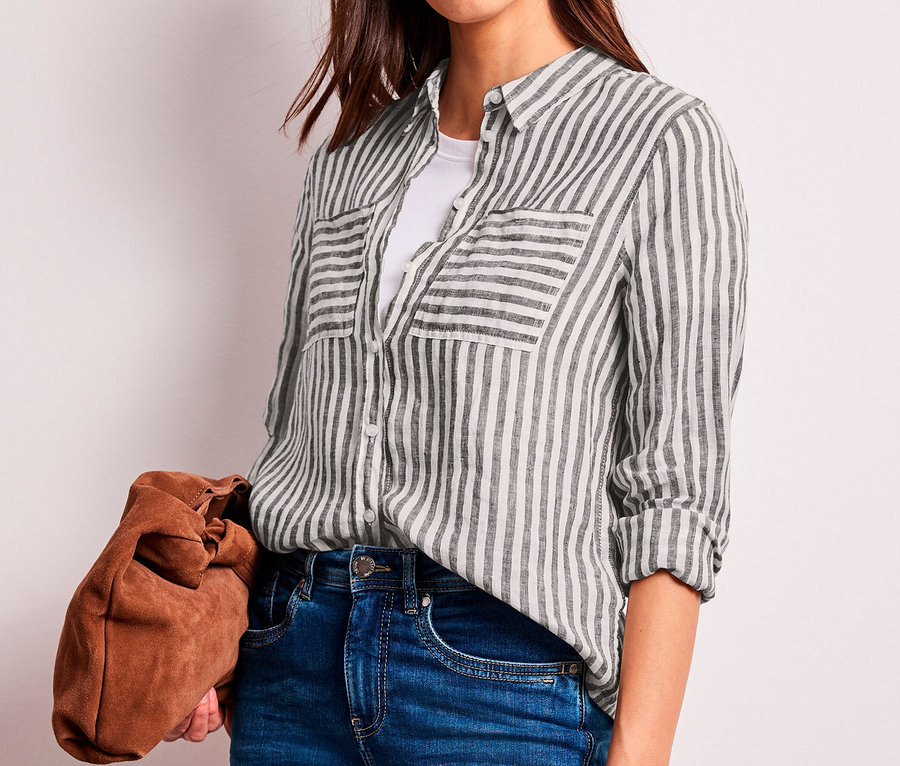 Kobieta w bluzce koszulowej Street One w ciemnobrązowo-białe paski, białym T-shircie i dżinsach, trzymająca brązową kopertówkę.
