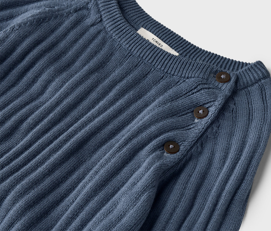 Zdjęcie z bliska prążkowanego, granatowego swetra z trzema guzikami przy kołnierzu.