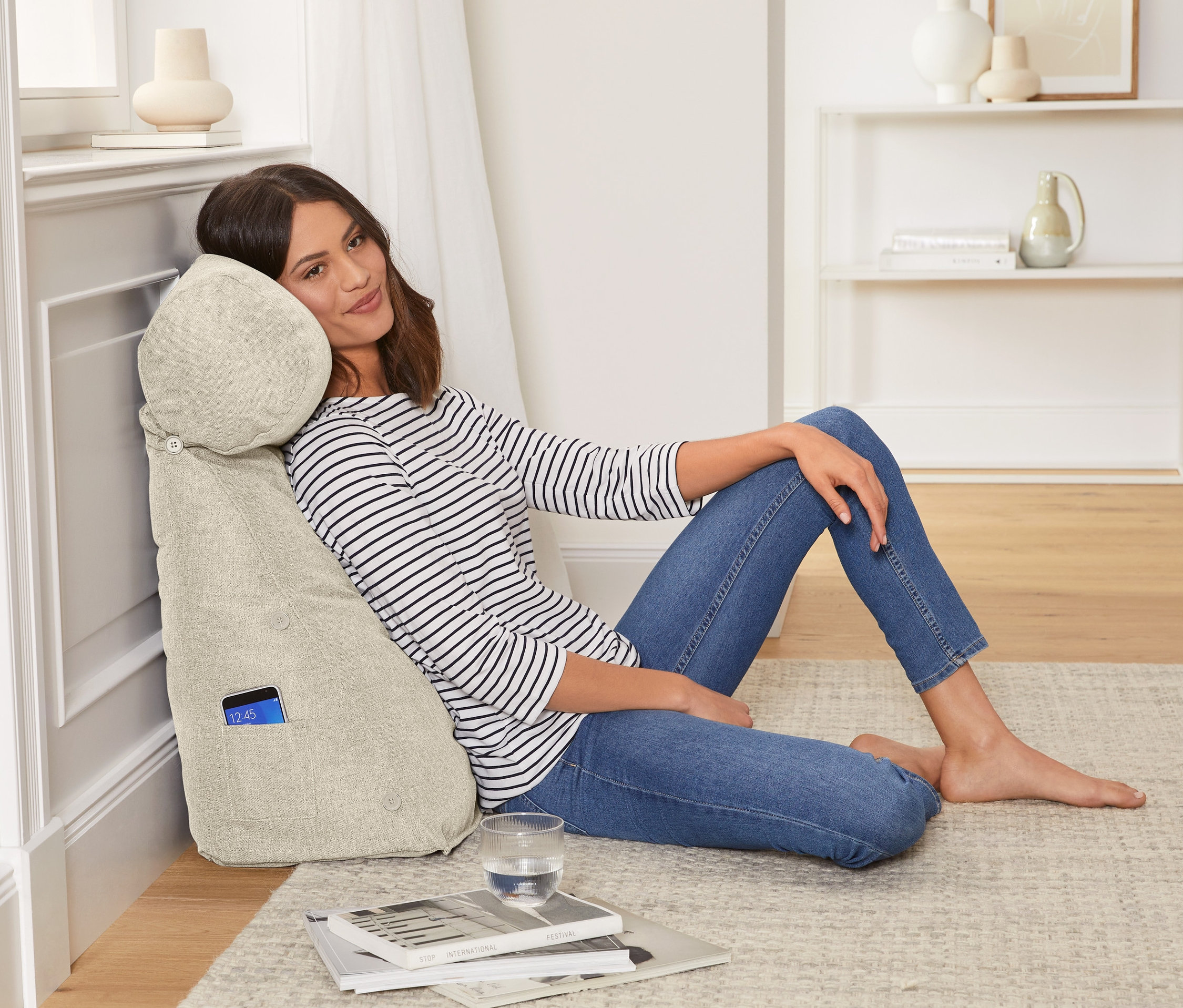 Kobieta siedzi na dywanie oparta o poduszkę-klin.