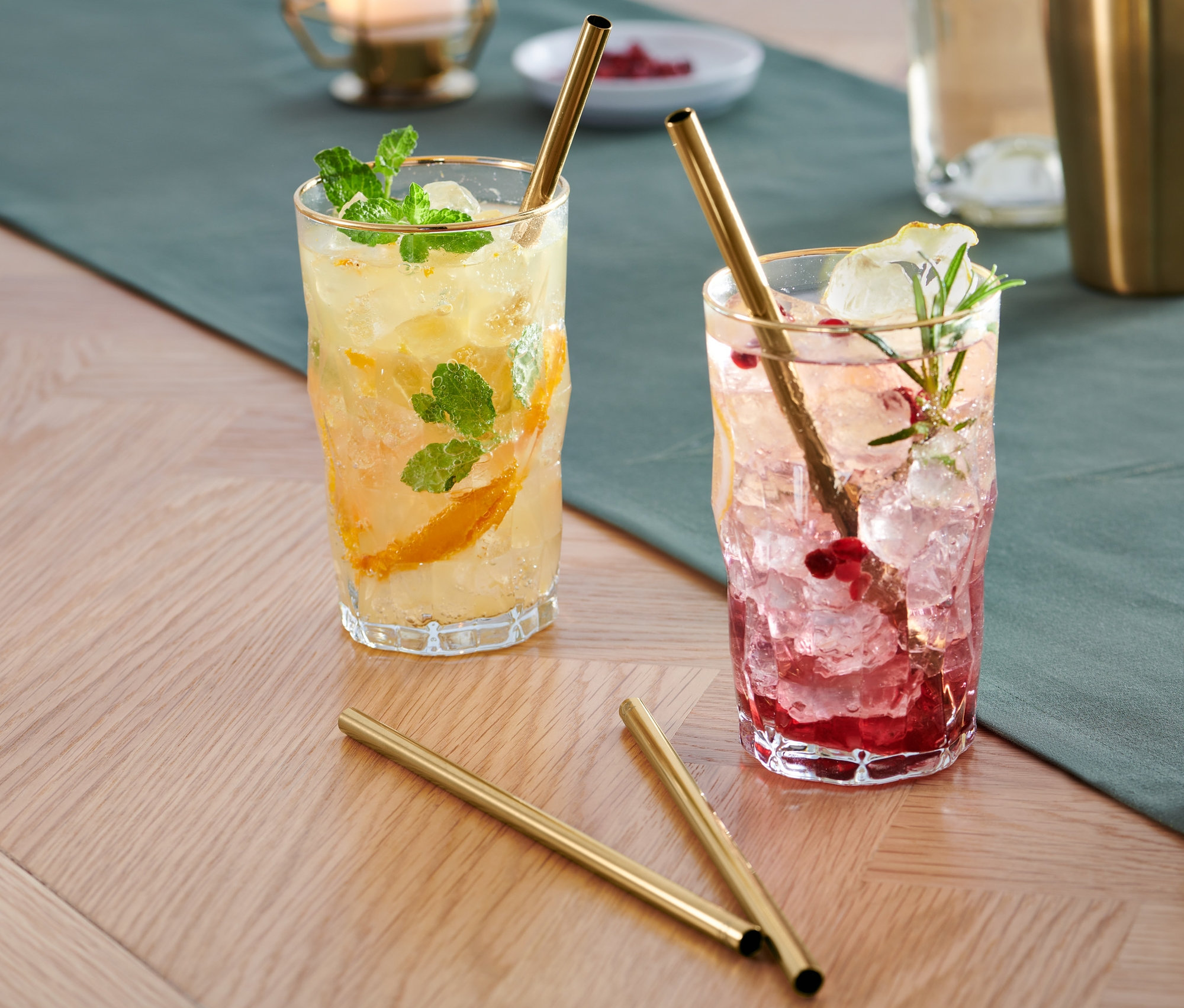 Dwa napoje z lodem i owocami w szklankach ze złotymi Metalowe słomki do picia, 4 sztuki stoją na stole.
