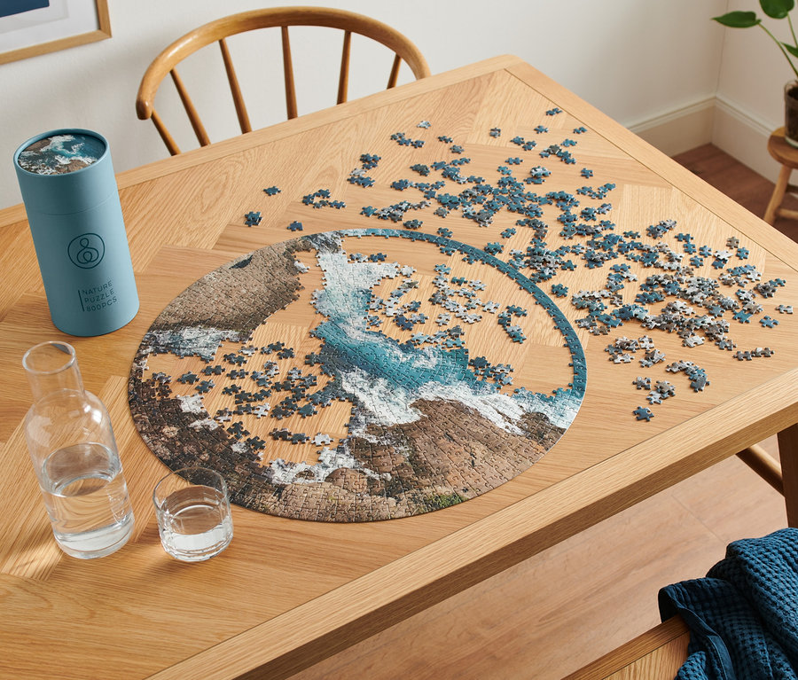 Na drewnianym stole leżą puzzle »Ocean« i wazon z wodą.