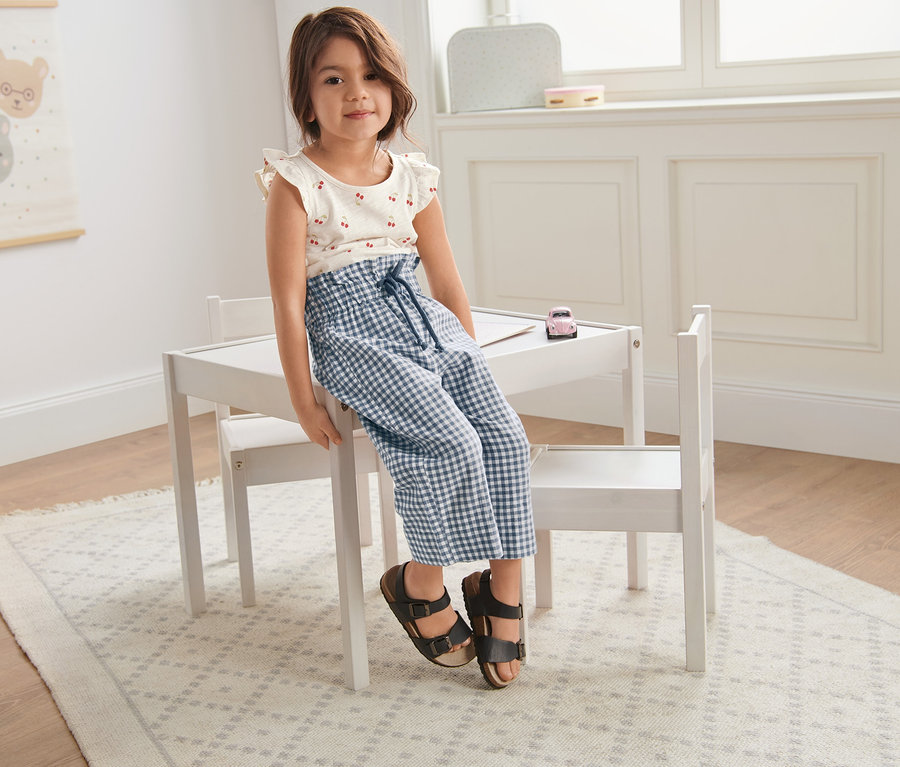 Dziewczynka siedzi na białym stole, ubrana w kuloty z lnem i koszulkę z 3-częściowego zestawu.