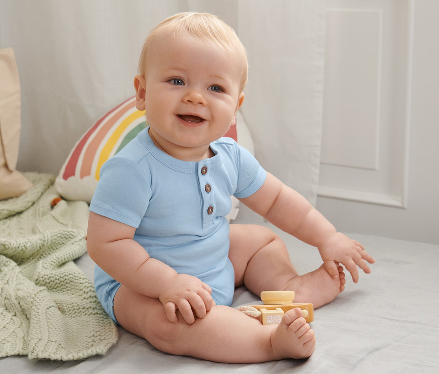 Uśmiechnięty niemowlę siedzi i ma na sobie niebieskie body z bawełny ekologicznej, 3 sztuki.