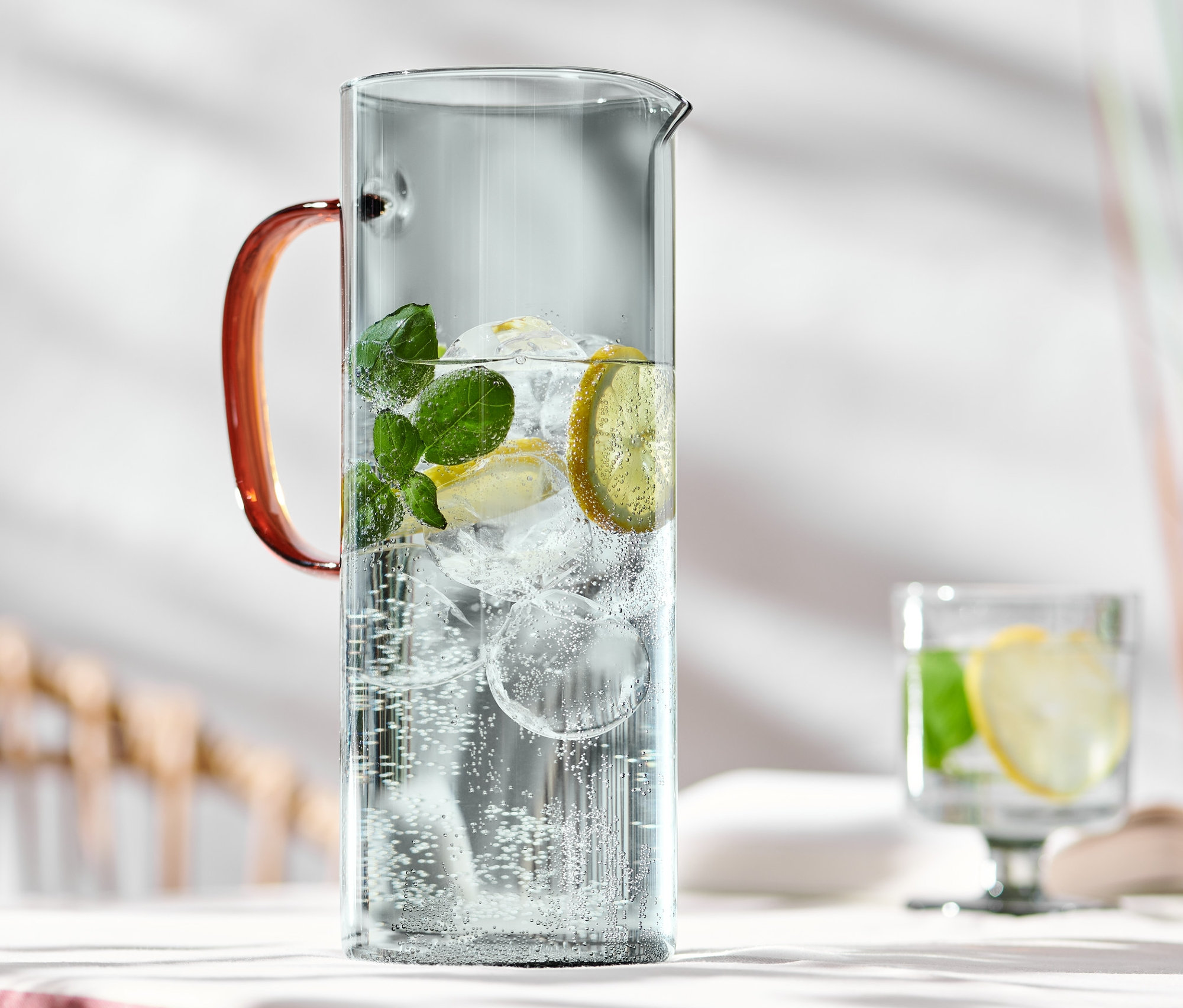 Szklany dzbanek z wodą, lodem, cytryną i miętą na stole.