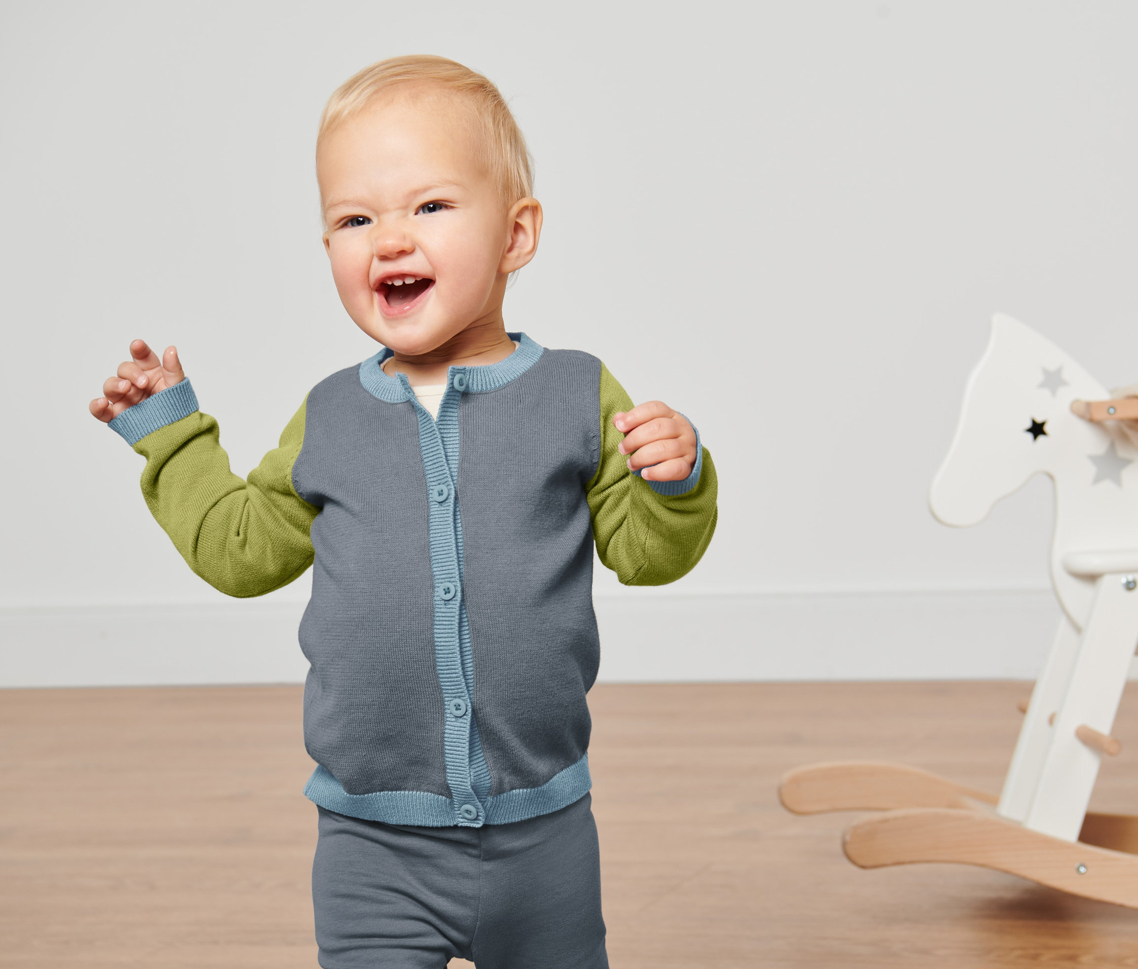 Uśmiechnięte dziecko macha rękami i ma na sobie rozpinany sweter .