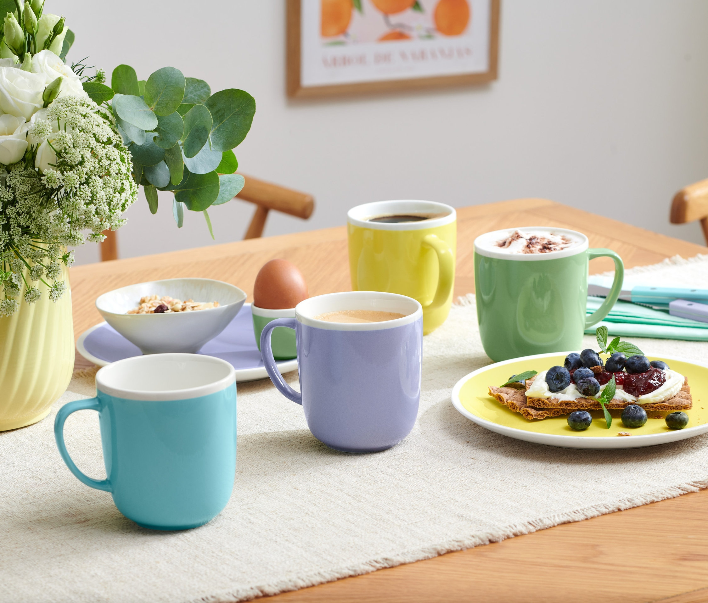 Cztery kubki w różnych kolorach stoją na stole z jedzeniem.