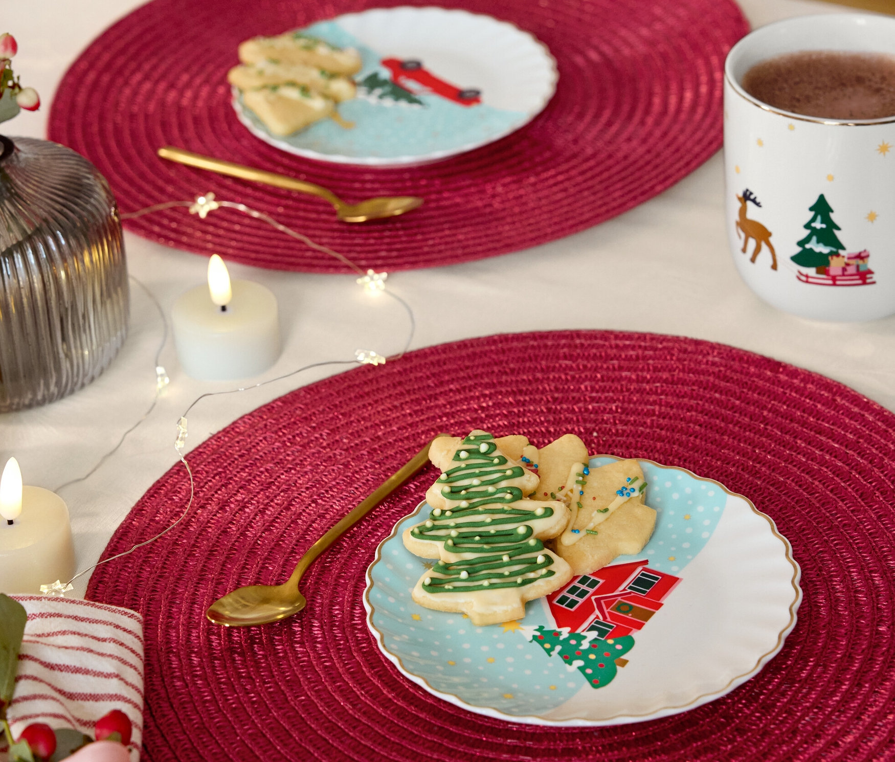 Dwa stoły z czerwonymi podkładkami, na nich talerzyki deserowe ze złotą dekoracją, foremki do ciastek i złote łyżeczki.