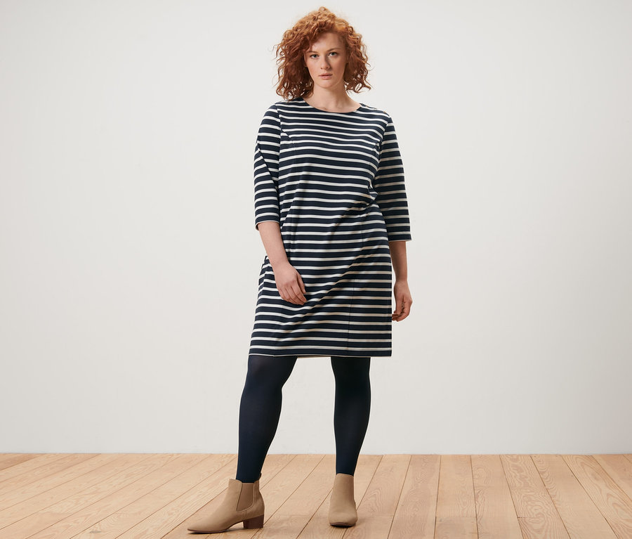 Kobieta stoi w sukience z dzianiny dresowej i cienkich rajstopach, 2 pary.