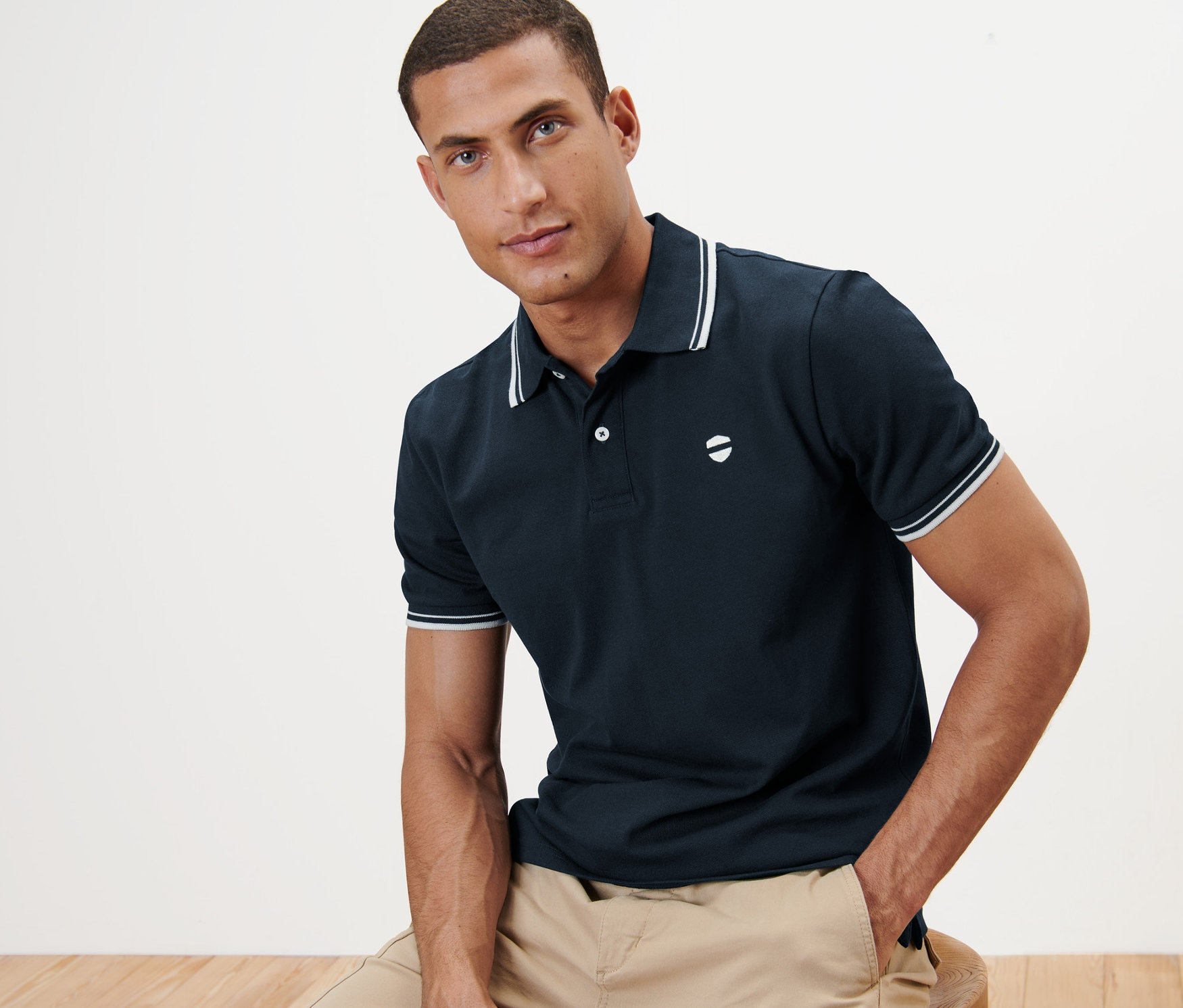 Mężczyzna siedzi i ma na sobie granatową koszulkę polo o splocie pique.