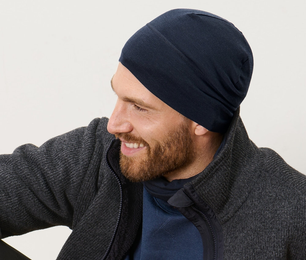 Mężczyzna siedzi na drewnianej podłodze i ma na sobie czapkę z zawartością wełny.