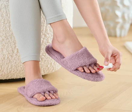 Kobieta maluje paznokcie u stóp w pantoflach do malowania paznokci i relaksu.
