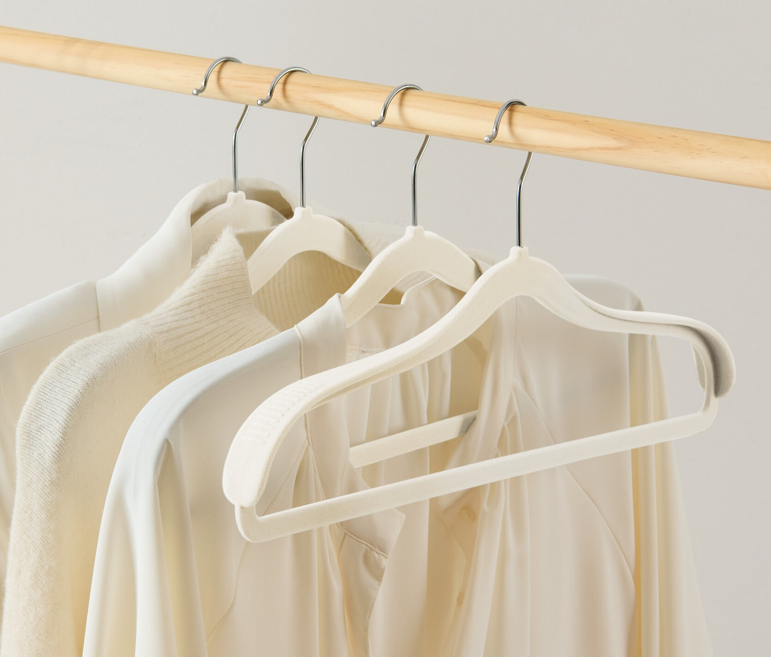 Cztery wieszaki na ubrania z pogrubioną okolicą ramion wiszą na drewnianym stojaku.