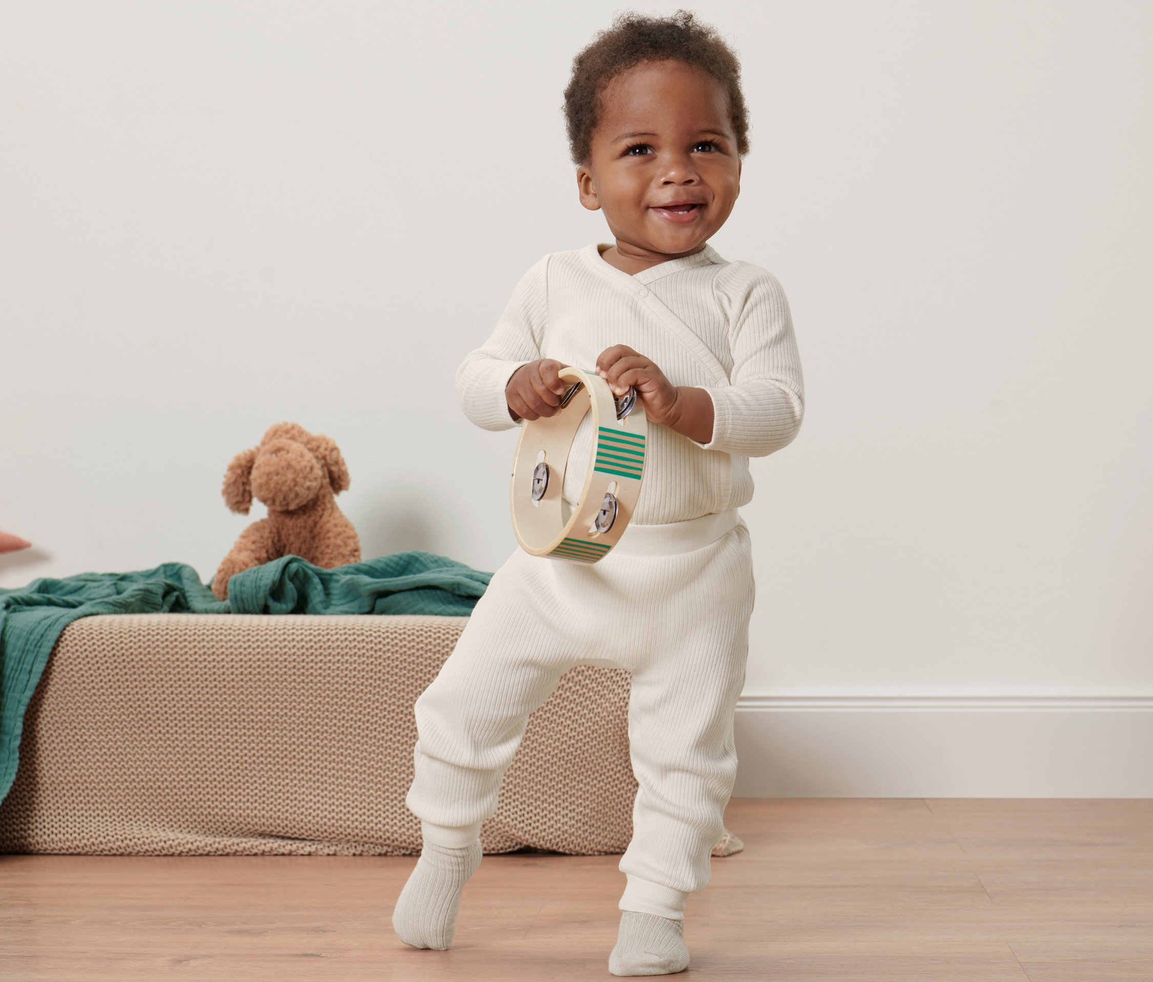 Uśmiechnięty czarnoskóry maluch trzyma tamburyn i stoi w spodniach z dzianiny.