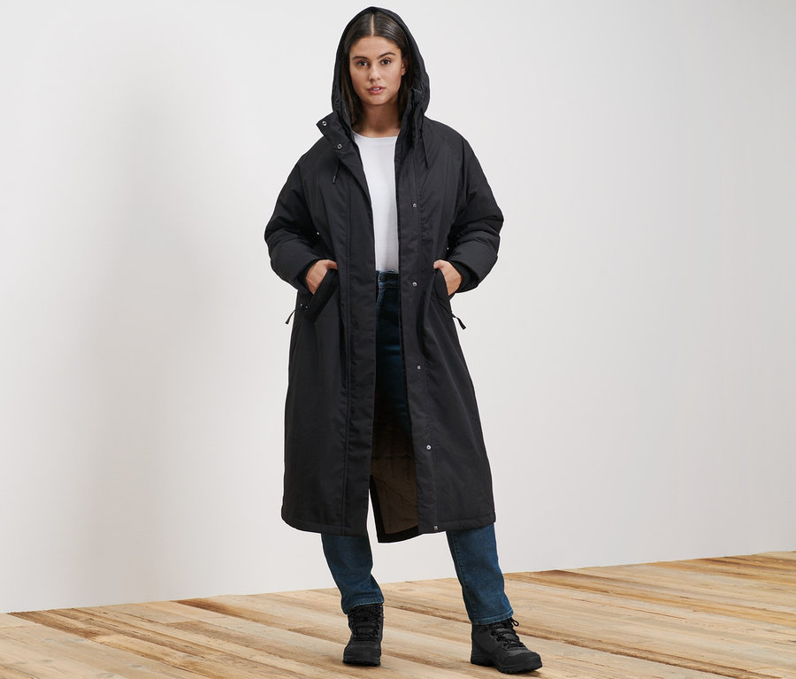 Kobieta stoi i ma na sobie wyjątkowo długi płaszcz zimowy oraz jeansy slim »Fit Emma« w kolorze dark blue denim.